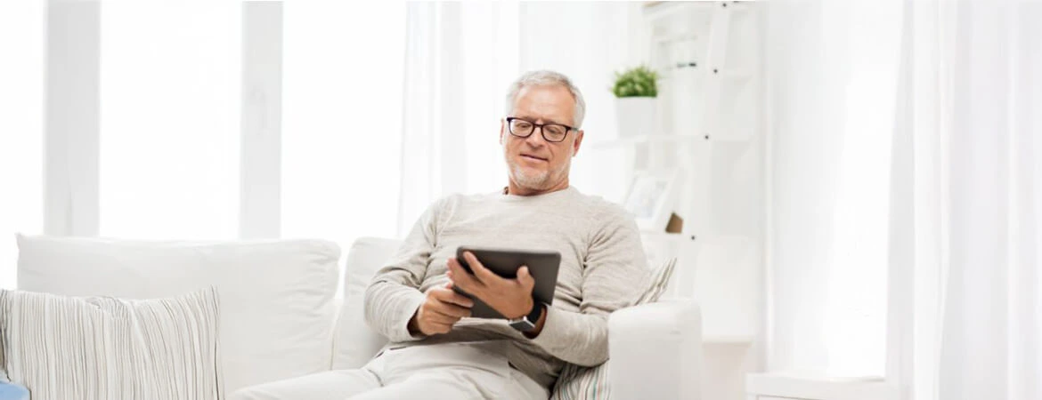 A man seated on a white sofa in a minimalist white-themed room, reading a tablet. The image illustrates a probate real estate representative reviewing essential terms. Reach out to Kid Breukelen Realty Group for expert help in understanding probate real estate.