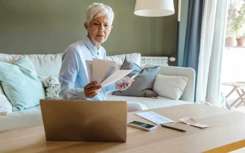 Reading bill on sofa with computer open in Broward